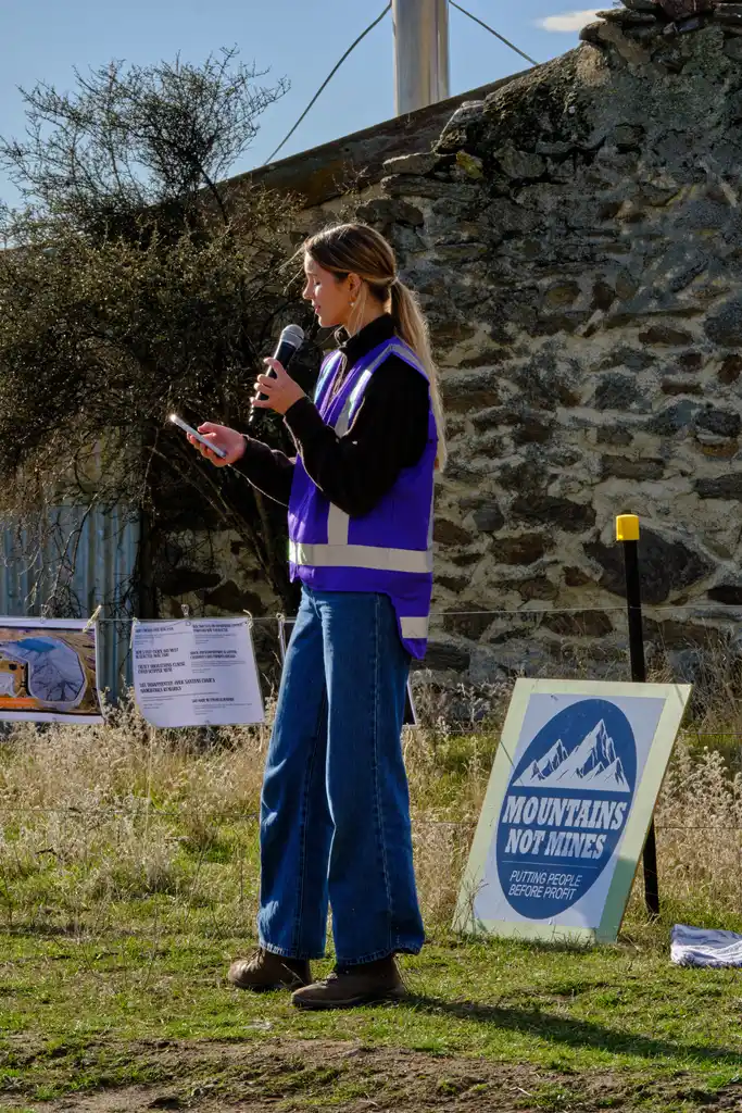Speaker addressing the Fool’s Gold Road event beside a Mountains Not Mines sign